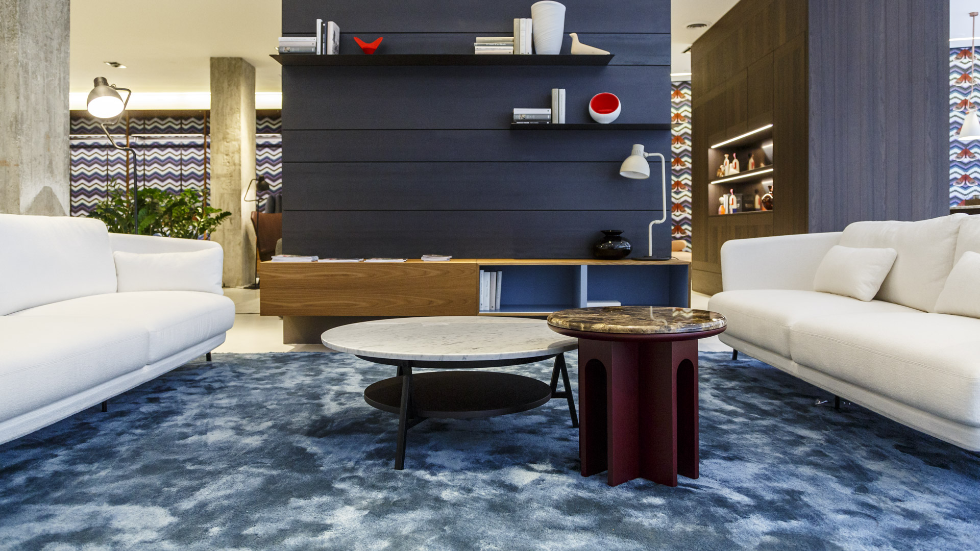 Shaded navy blue rug in a living room with white sofas and marble side tables